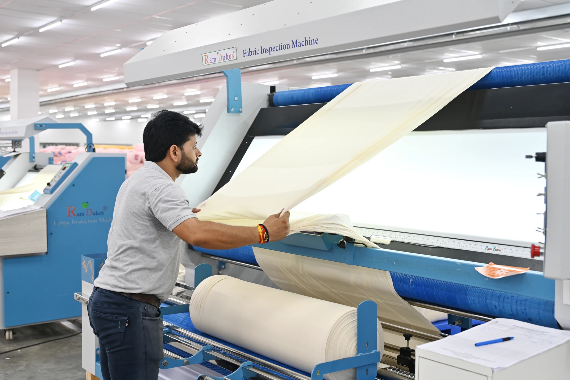An operator checks fabric at an illuminated inspection machine