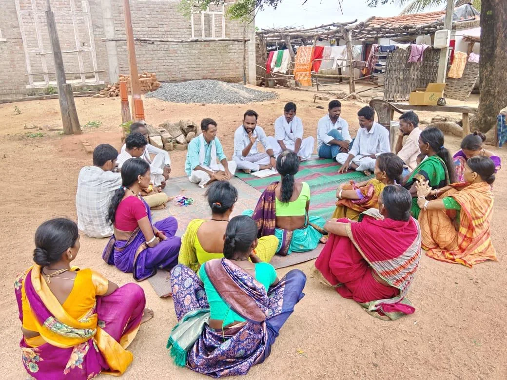 A group sits in a circle for a discussion in a village courtyard